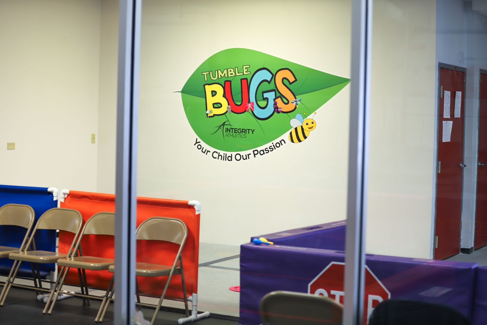 Indoor room with a green “Bugs” wall sign, folding chairs, and tables with red and purple tablecloths.