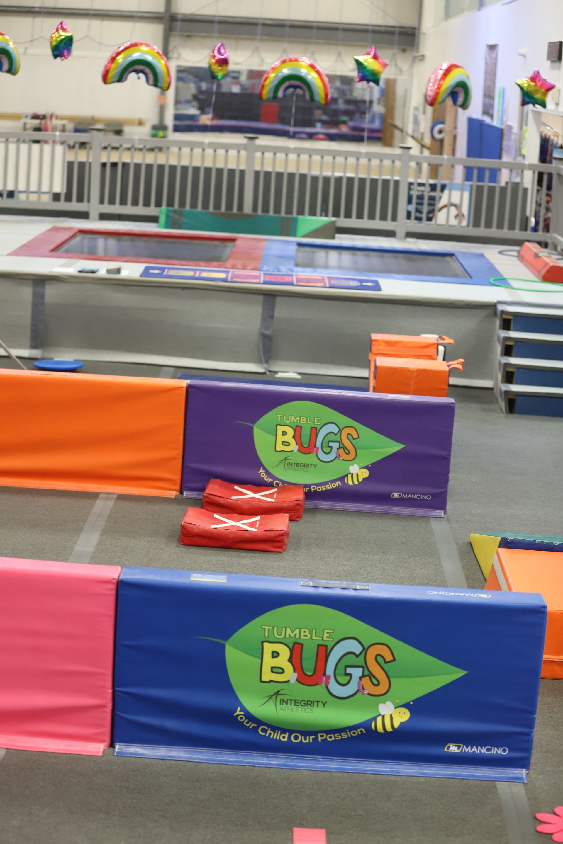 Bright indoor play area with colorful bug-themed barriers, ramps, and rainbow wall decorations