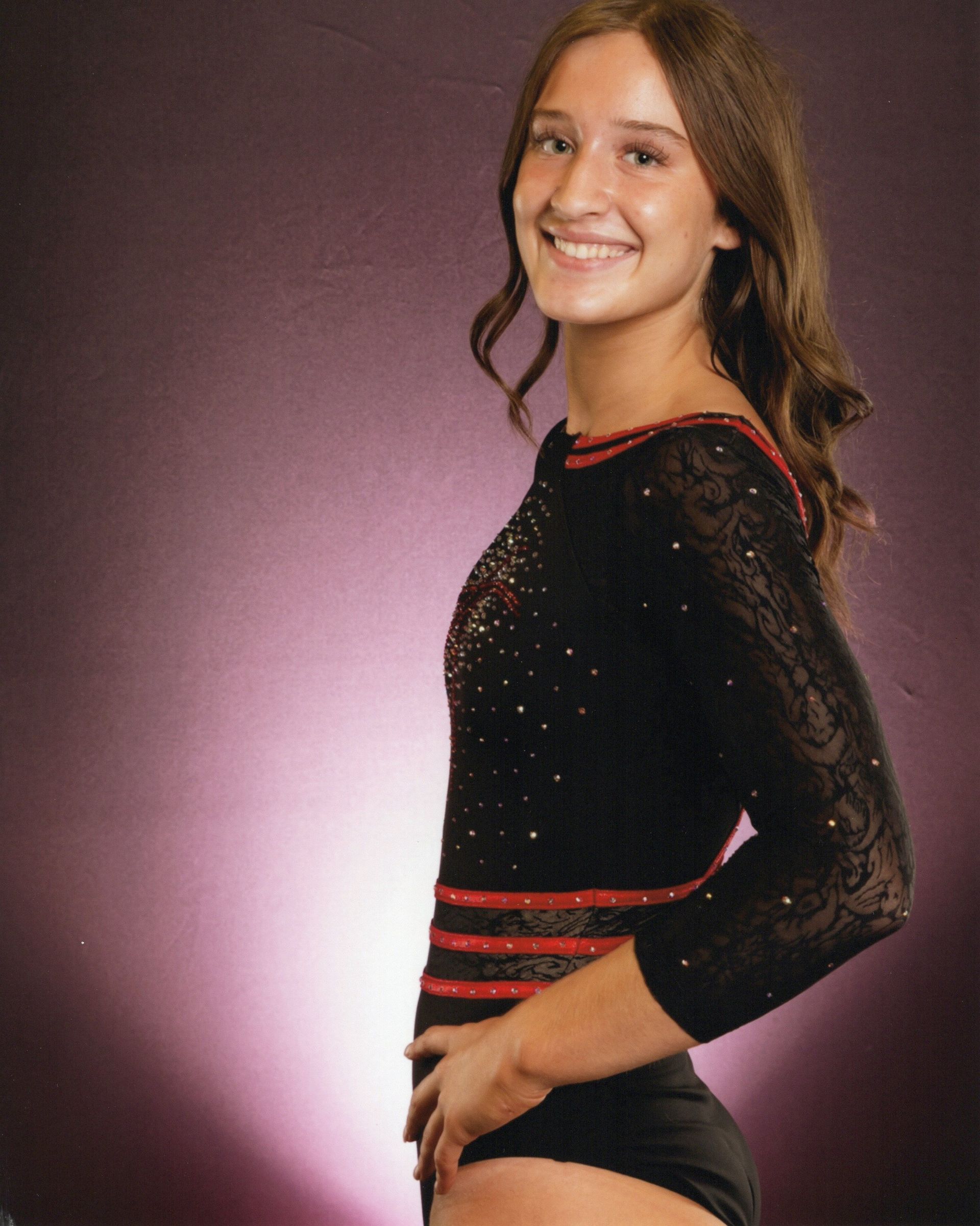 Woman in a black and red dance outfit smiling against a purple studio backdrop