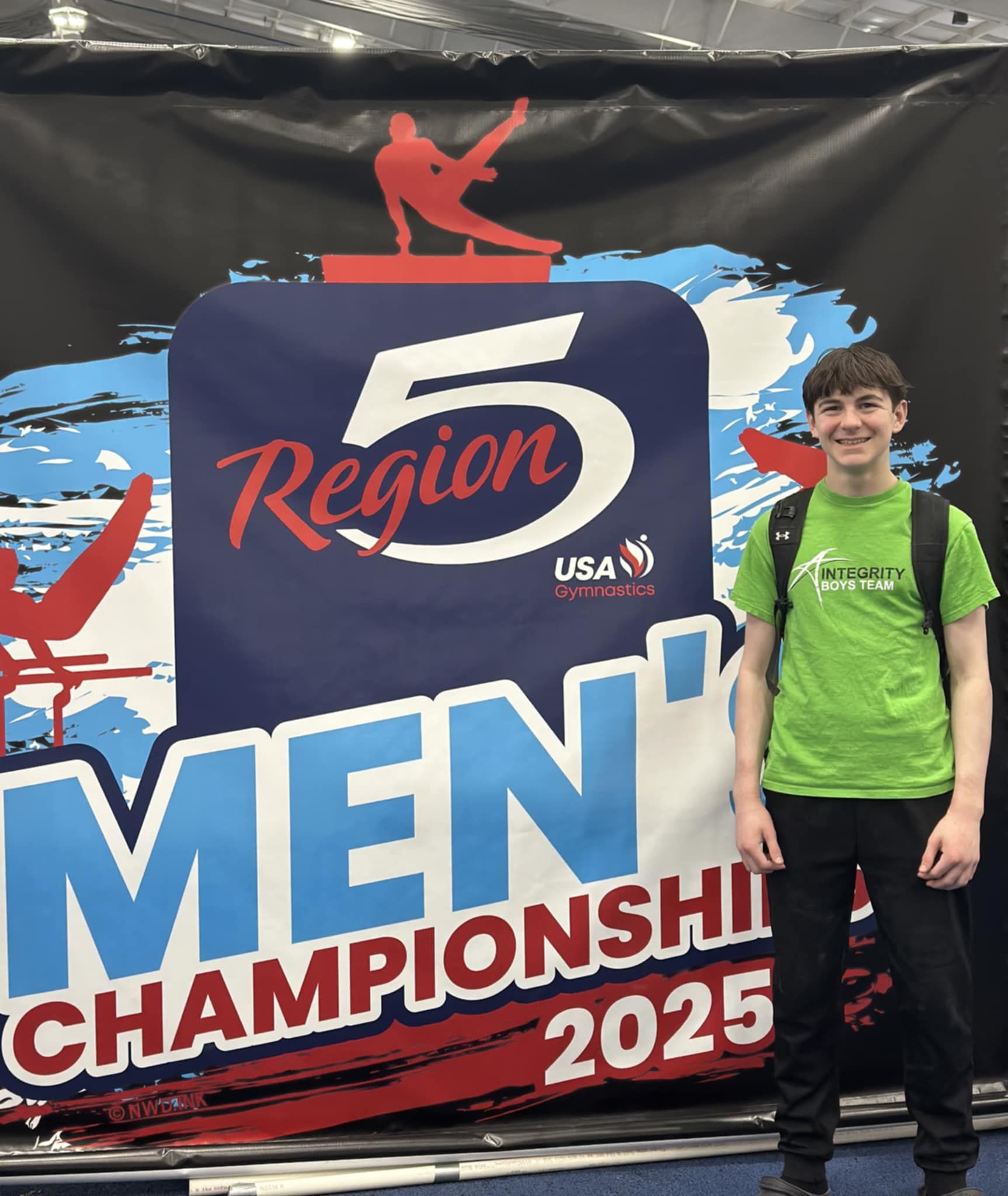 Young athlete in green shirt standing beside a 5 Region Men’s Championship 2025 banner