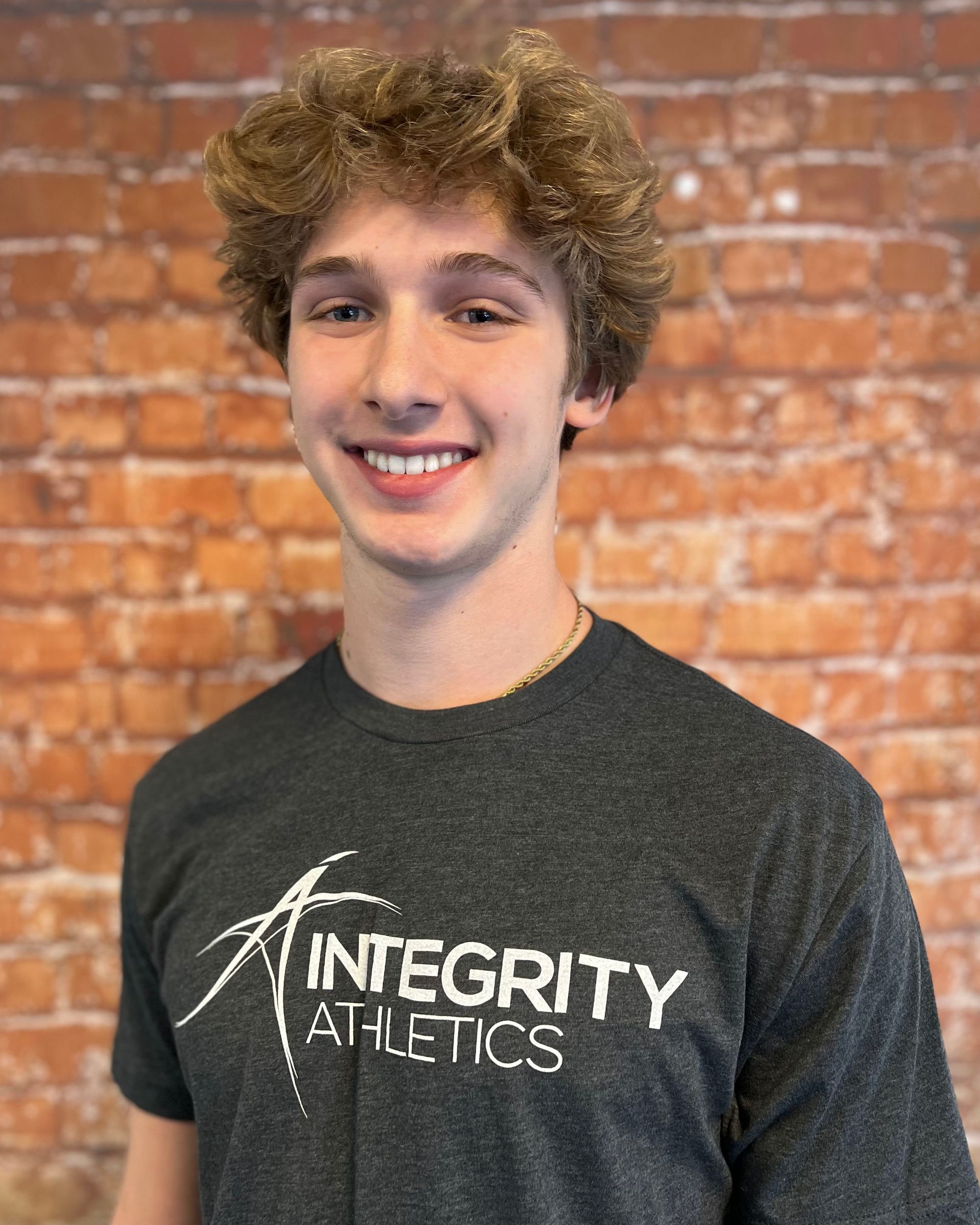 Smiling person in a black Integrity Athletics T-shirt against a brick wall backdrop
