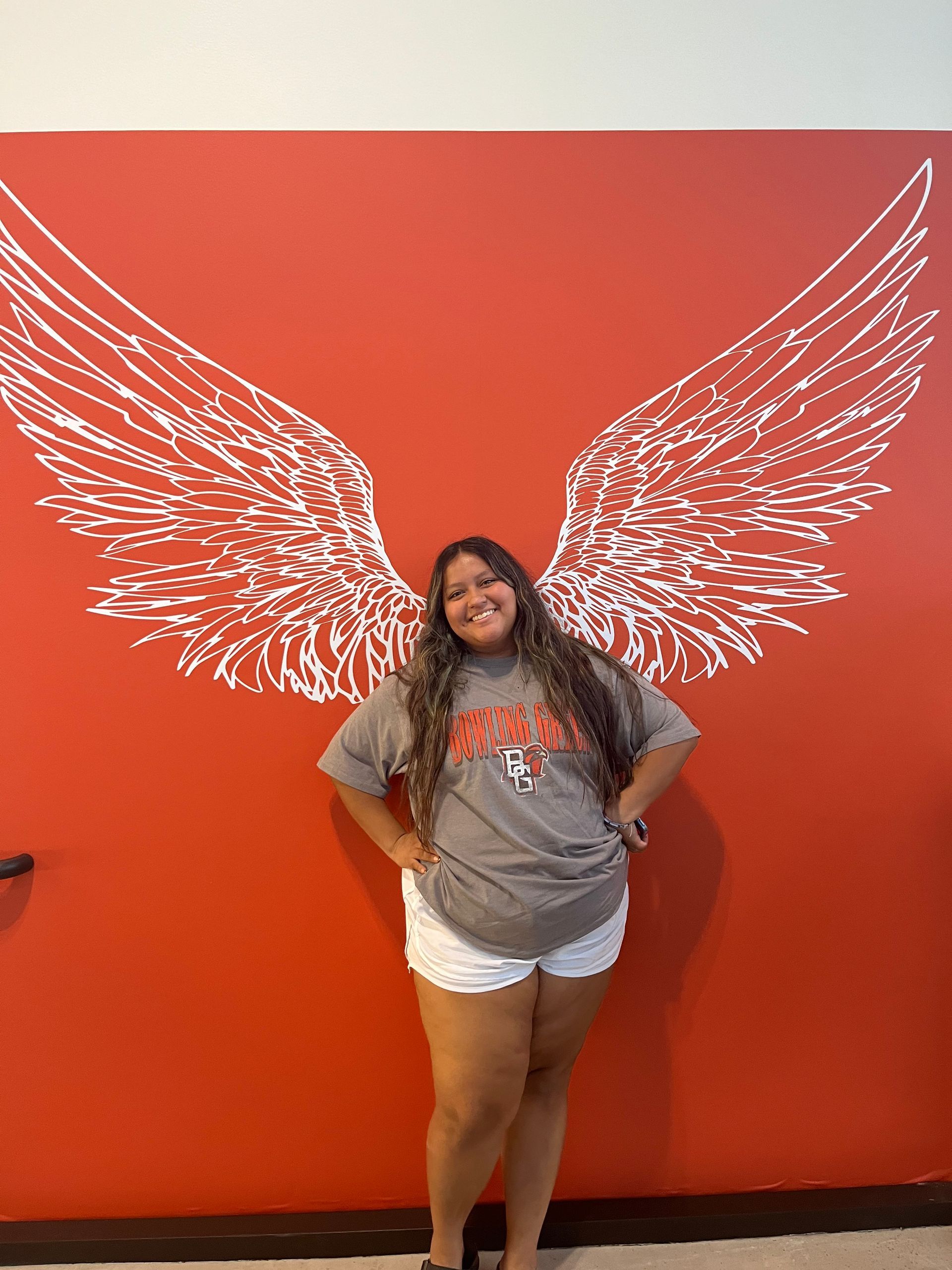 Person posing in front of a red wall with white wing graffiti.