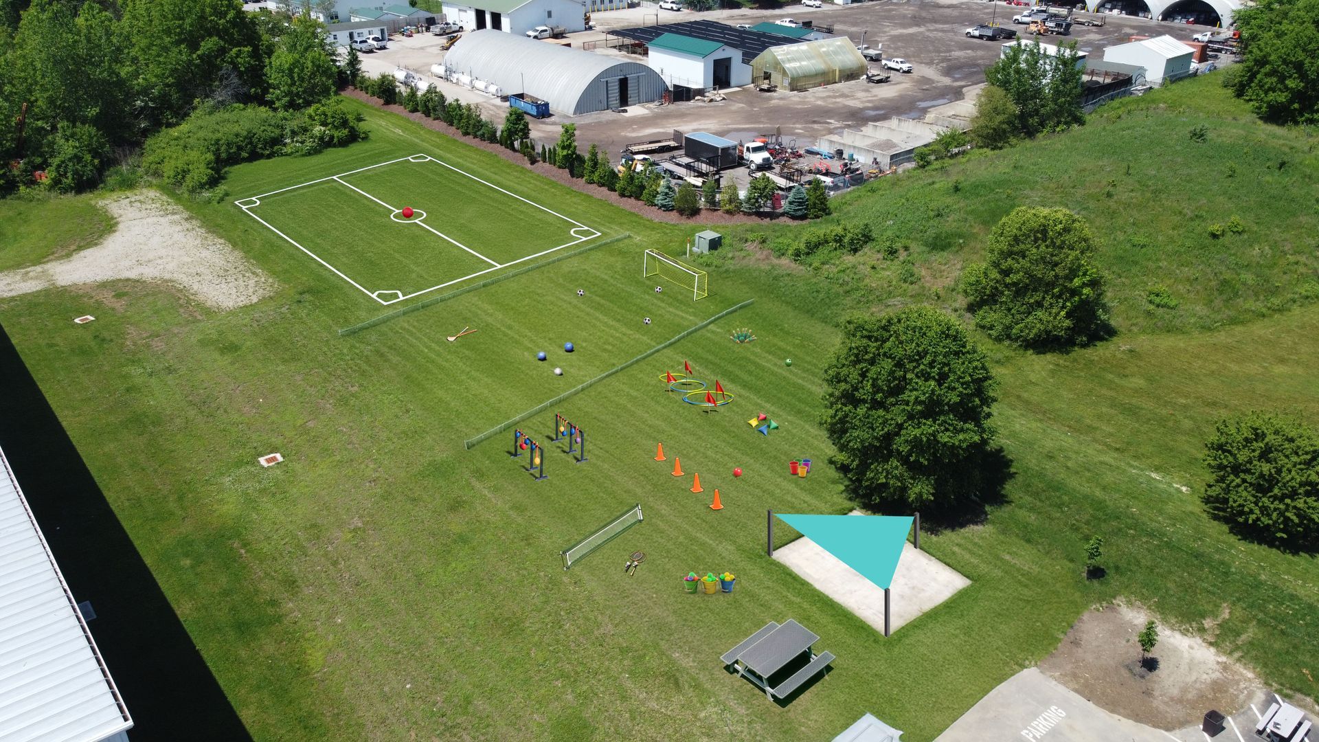 Aerial view of a grassy park with people near a small white tent and volleyball court.