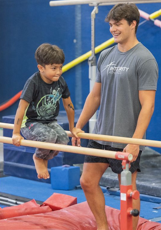 A man is helping a young girl do a handstand on a blue mat