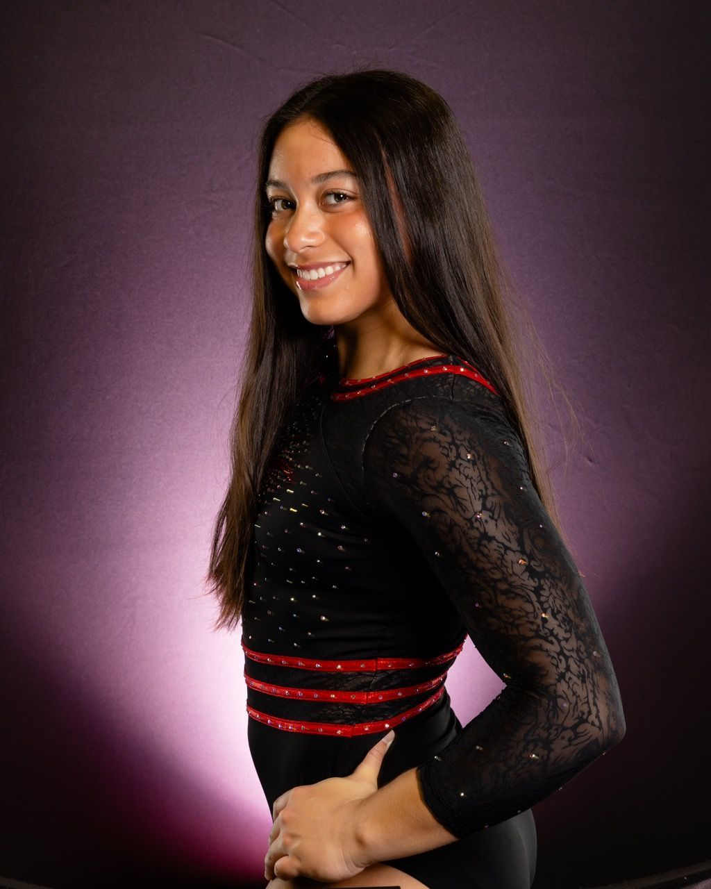Smiling woman in black and red dress, posing against a purple studio backdrop