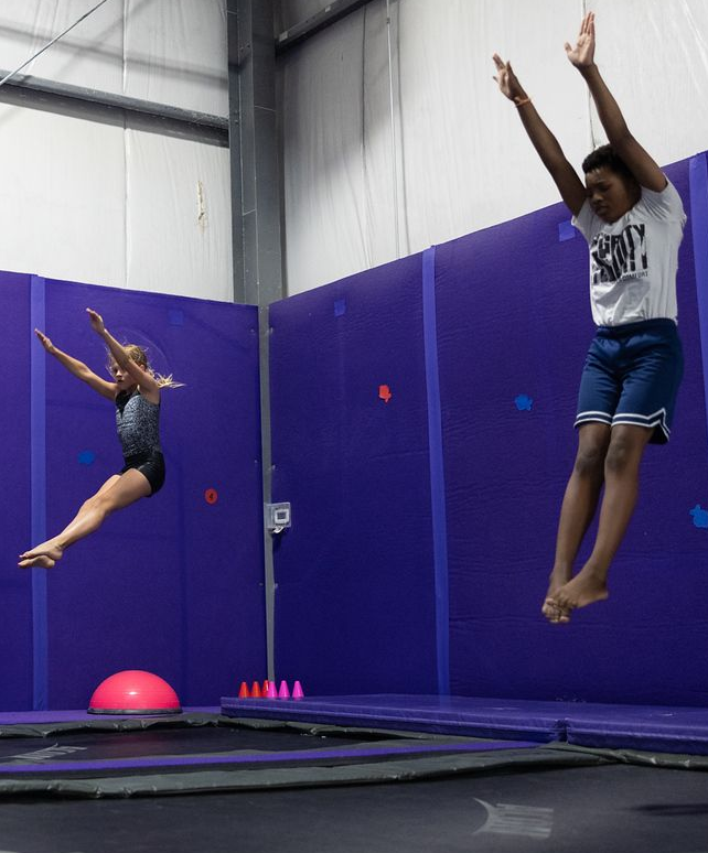 A woman in a purple shirt is helping a little girl on a balance beam.