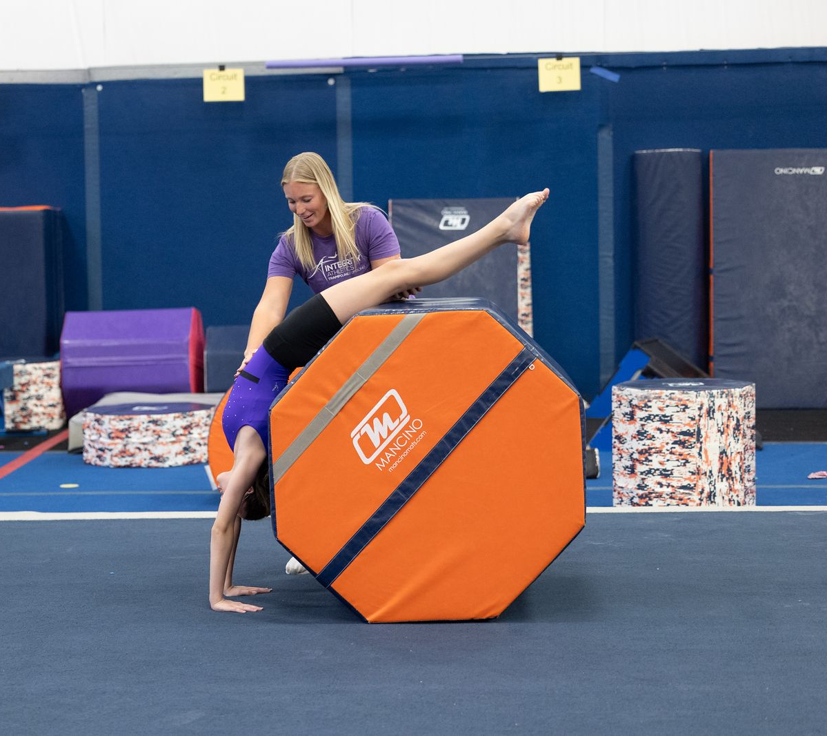 A young girl is doing a handstand on a blue mat.