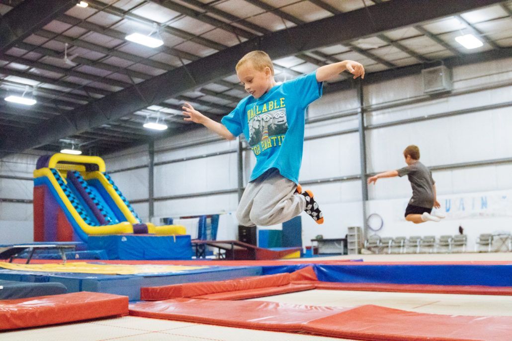 Child jumping on trampoline in an indoor gym, with colorful inflatable slides and another child in the background