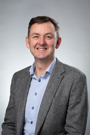 A man in a suit and blue shirt is smiling for the camera.