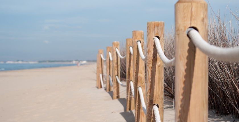 A wooden fence leading to a beach with a white railing.