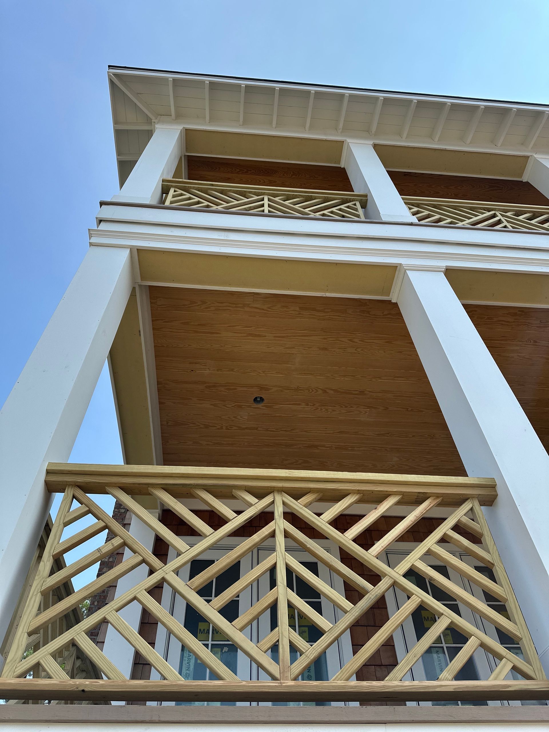 Multi-story building with white columns, wooden balconies, and intricate railing against a blue sky.