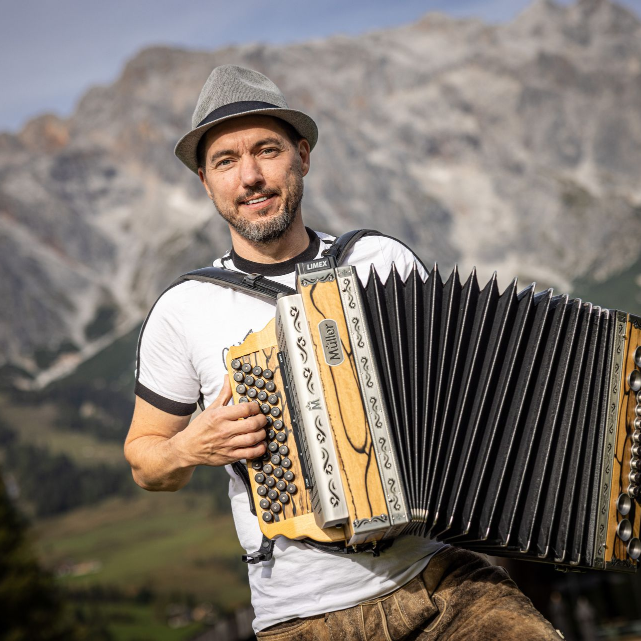 Mann mit Hut spielt im Freien Akkordeon vor der Kulisse von Bergen