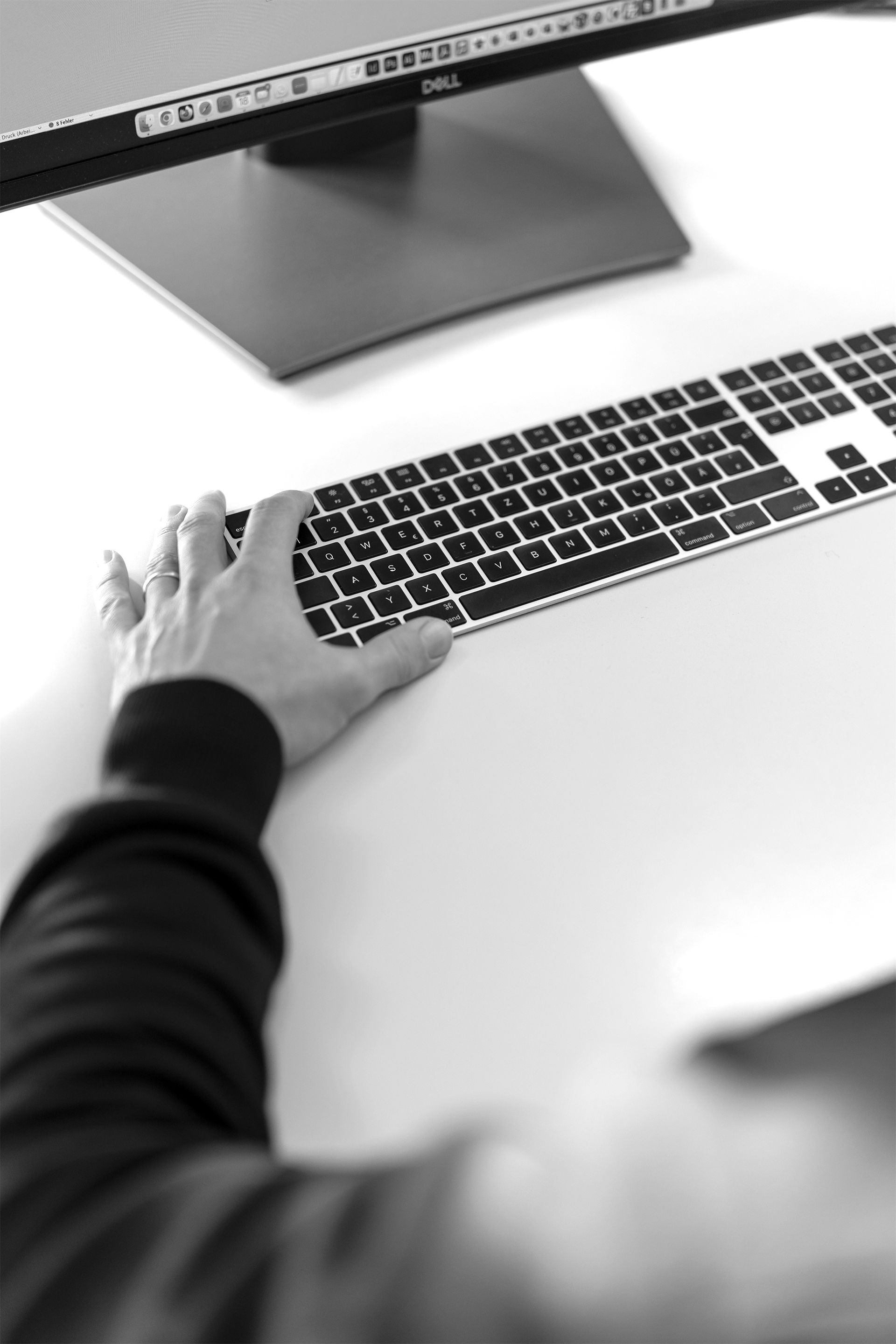 Schwarz-Weiß Bild einer Tastatur mit linker Hand im Hintergrund ein angeschnittener Bildschirm. Ein Grafikarbeitsplatz as2