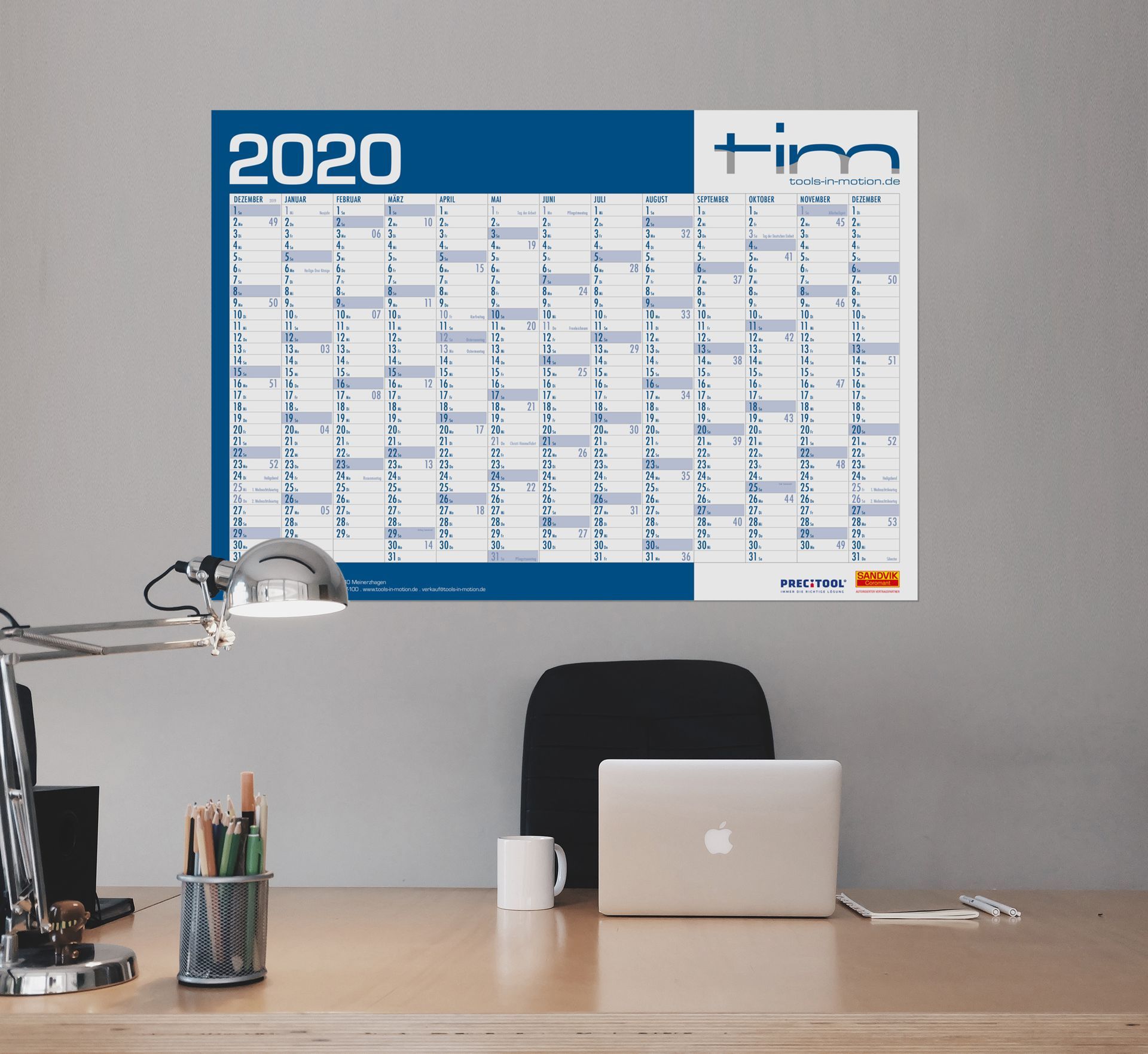 Weißer Wandalender mit blauen Grafikelementen hinter Schreibtisch mit Lampe. Grafikdesign von as2 aus Reutlingen.
