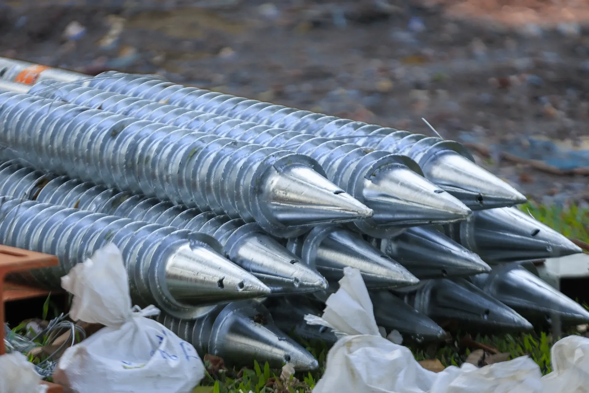 Stacked silver metal auger drill bits lying outdoors on the ground — Ground Screws SEQ Pty Ltd In Meridan Plains, QLD
