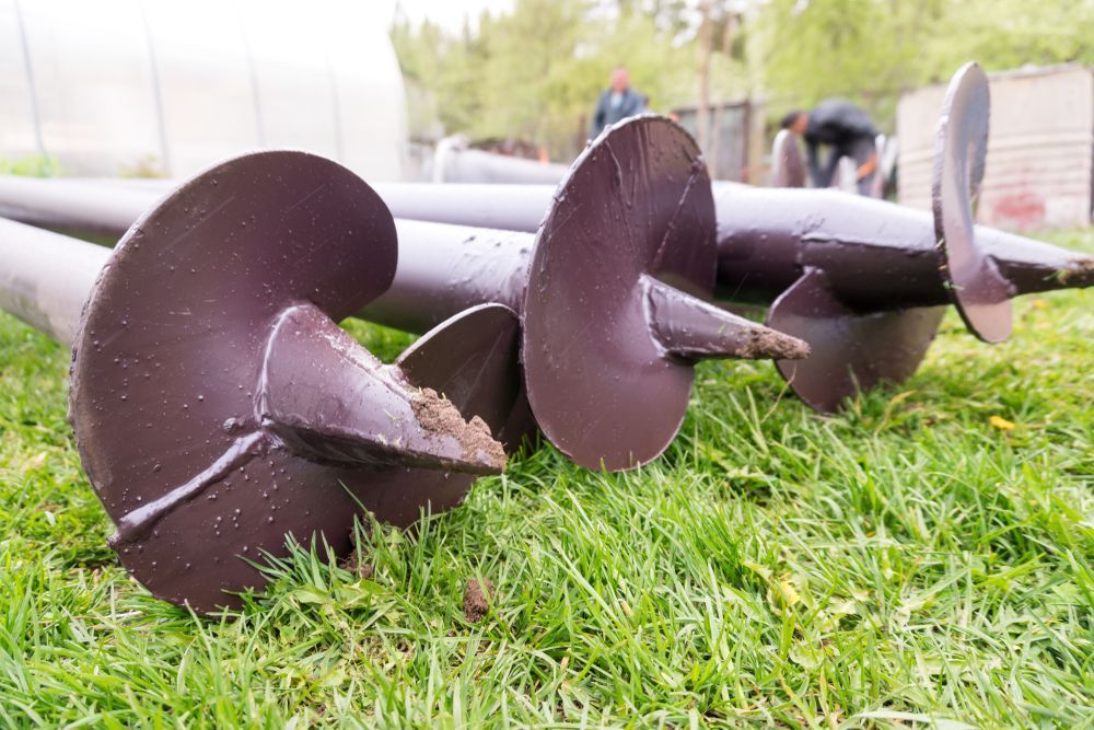 Three Large Metal Auger Drill Bits Lying on Grass Outdoors — Ground Screws SEQ Pty Ltd In Meridan Plains, QLD