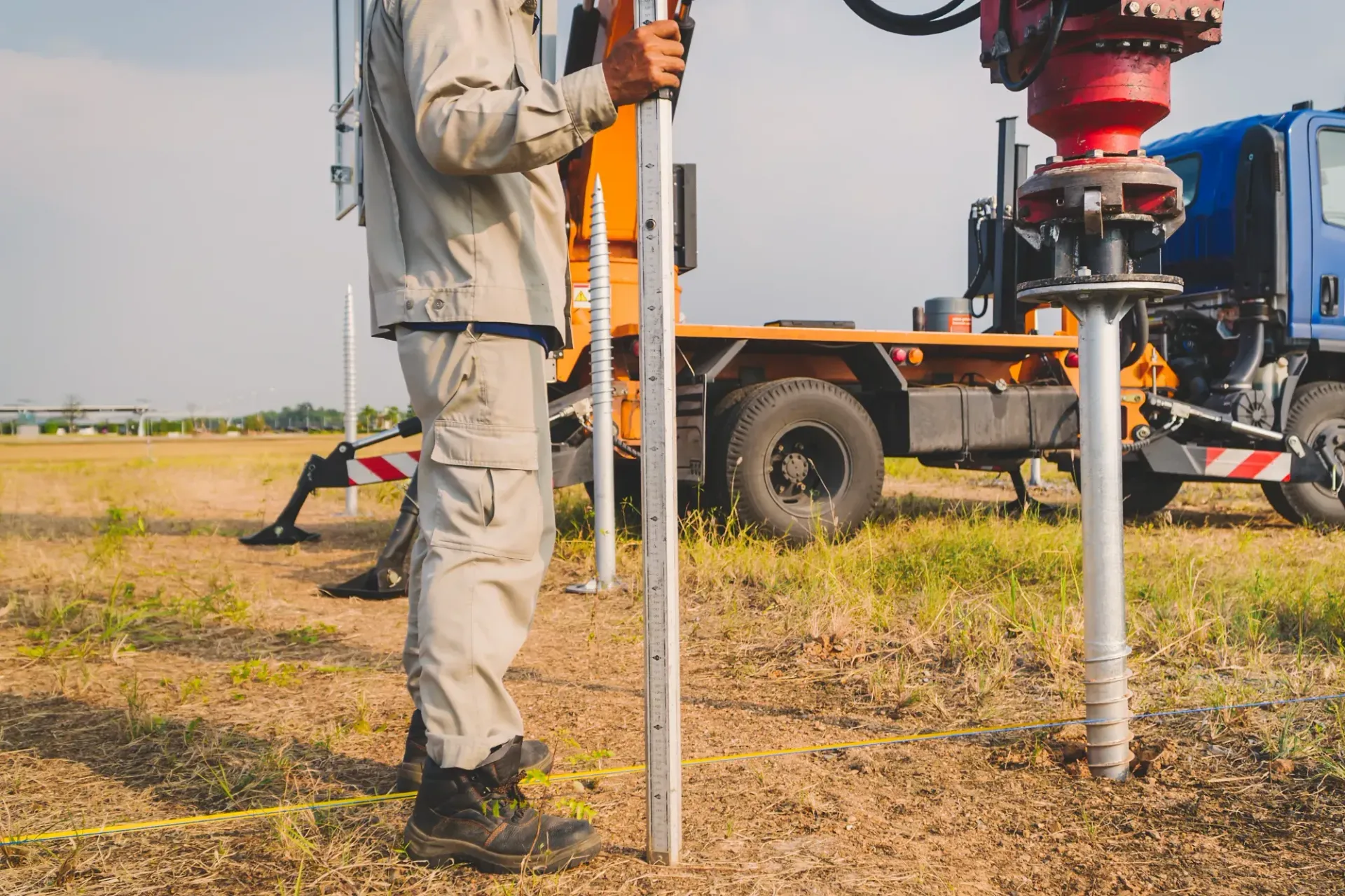 Worker Drilling a Test Hole Beside a Truck-mounted Rig in a Dry Field — Ground Screws SEQ Pty Ltd In Hervey Bay, QLD
