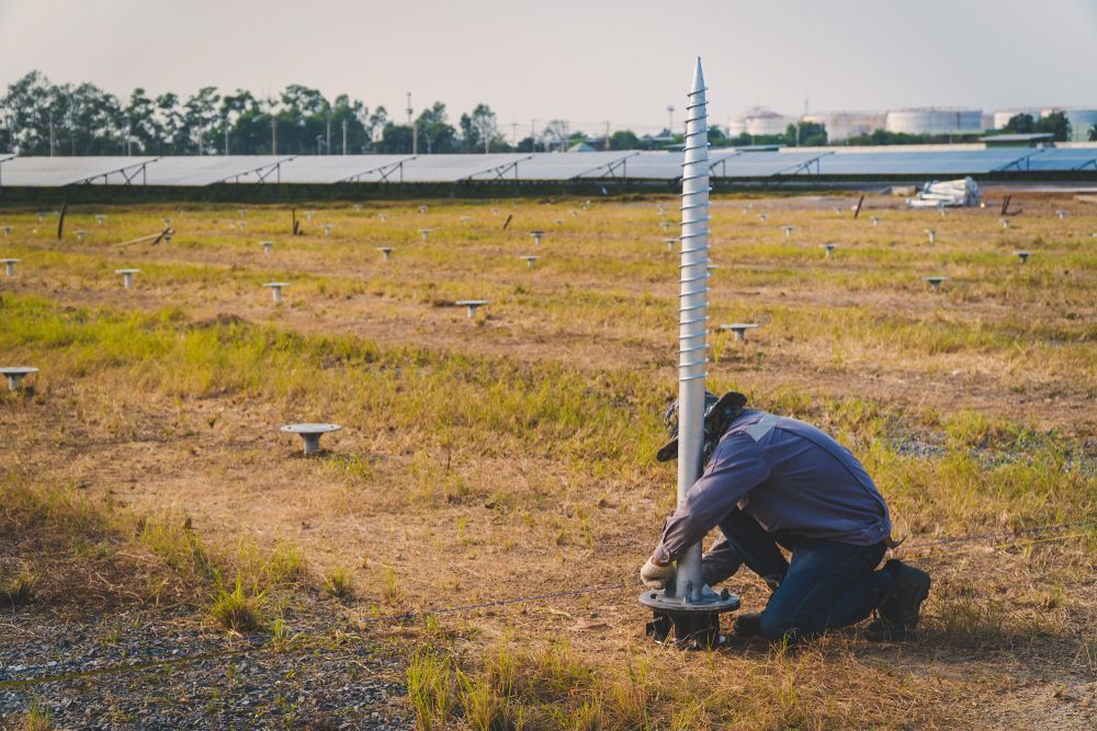 Person Kneeling in a Dry Field Beside a Tall White Measuring Pole — Ground Screws SEQ Pty Ltd In Meridan Plains, QLD