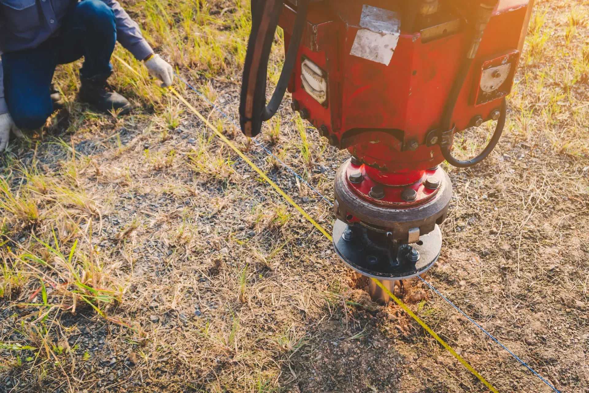Worker Using a Red Surveying Machine to Mark a LINE on Dry Ground — Ground Screws SEQ Pty Ltd In Caboolture, QLD
