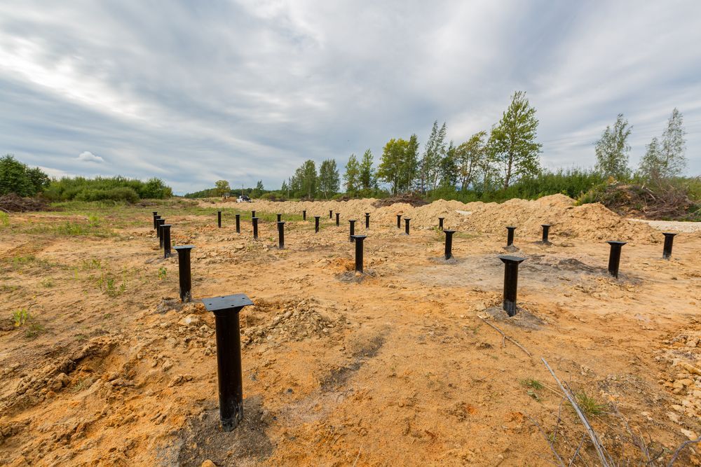 Sandy Construction Site With Rows of Black Posts Under a Cloudy Sky and Trees — Ground Screws SEQ Pty Ltd In Brisbane, QLD