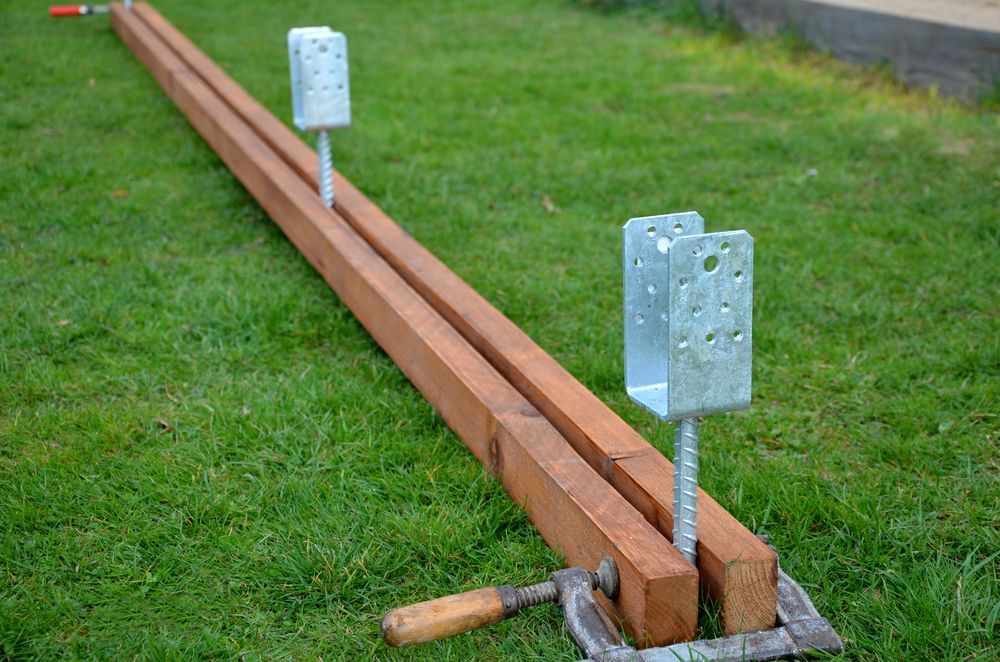 Long Wooden Beams Aligned on Grass Beside Metal Bracket Anchors — Ground Screws SEQ Pty Ltd In Meridan Plains, QLD