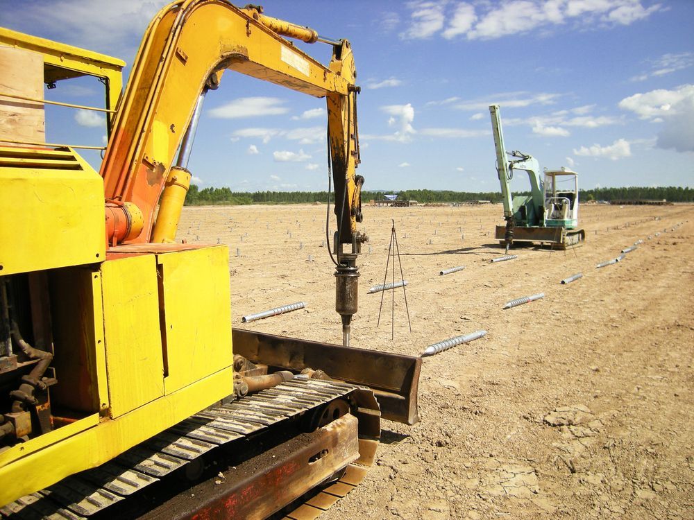 Yellow Excavator Drilling in a Sandy Construction Site With Another — Ground Screws SEQ Pty Ltd In Hervey Bay, QLD