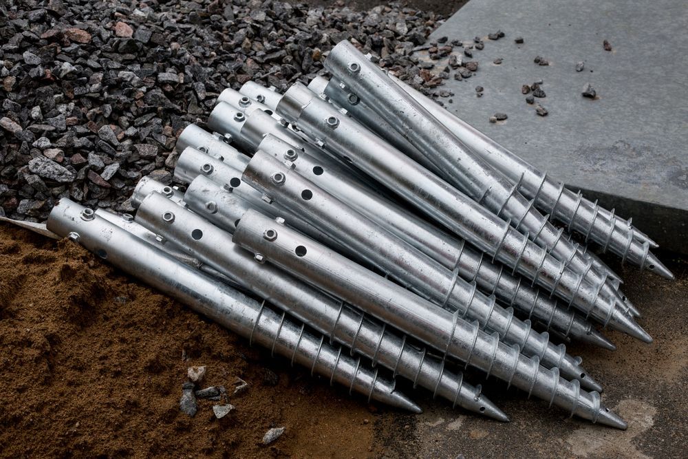 Stack Of Silver Metal Conical Spikes on Gravel Beside a Concrete Surface — Ground Screws SEQ Pty Ltd In Meridan Plains, QLD