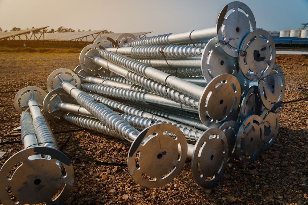 Stacked Metal Utility Poles With Circular BASE Plates Lying on Gravel — Ground Screws SEQ Pty Ltd In Meridan Plains, QLD
