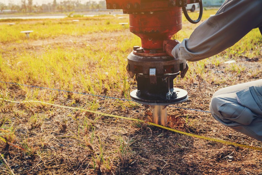 Worker Using a Surveying Instrument to Measure Land in a Field at Sunset — Ground Screws SEQ Pty Ltd In Meridan Plains, QLD