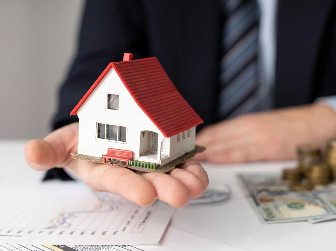 A man is holding a small model house in his hand.