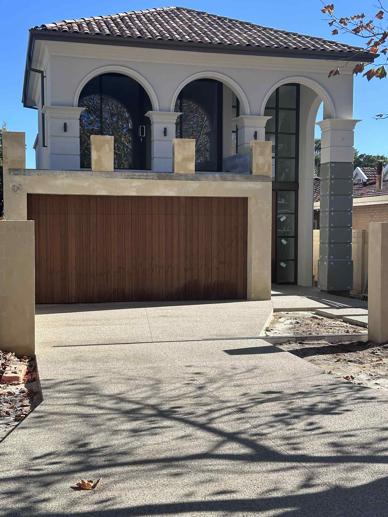 Modern white building with coral exposed aggregate driveway, brick fence, trees, and a cloudy sky 
