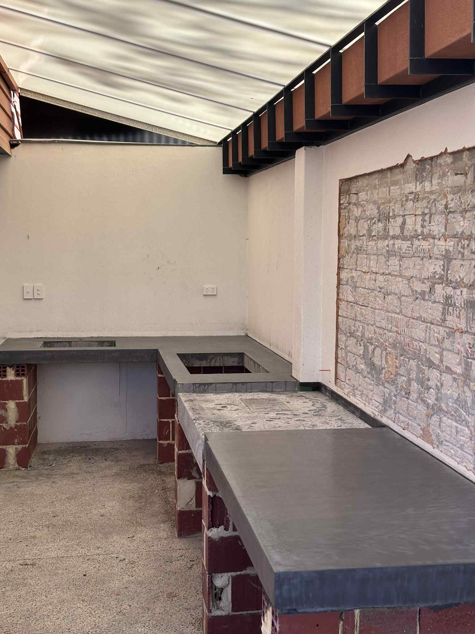 Outdoor kitchen with gray concrete countertop, brick supports, and white walls under a canopy.