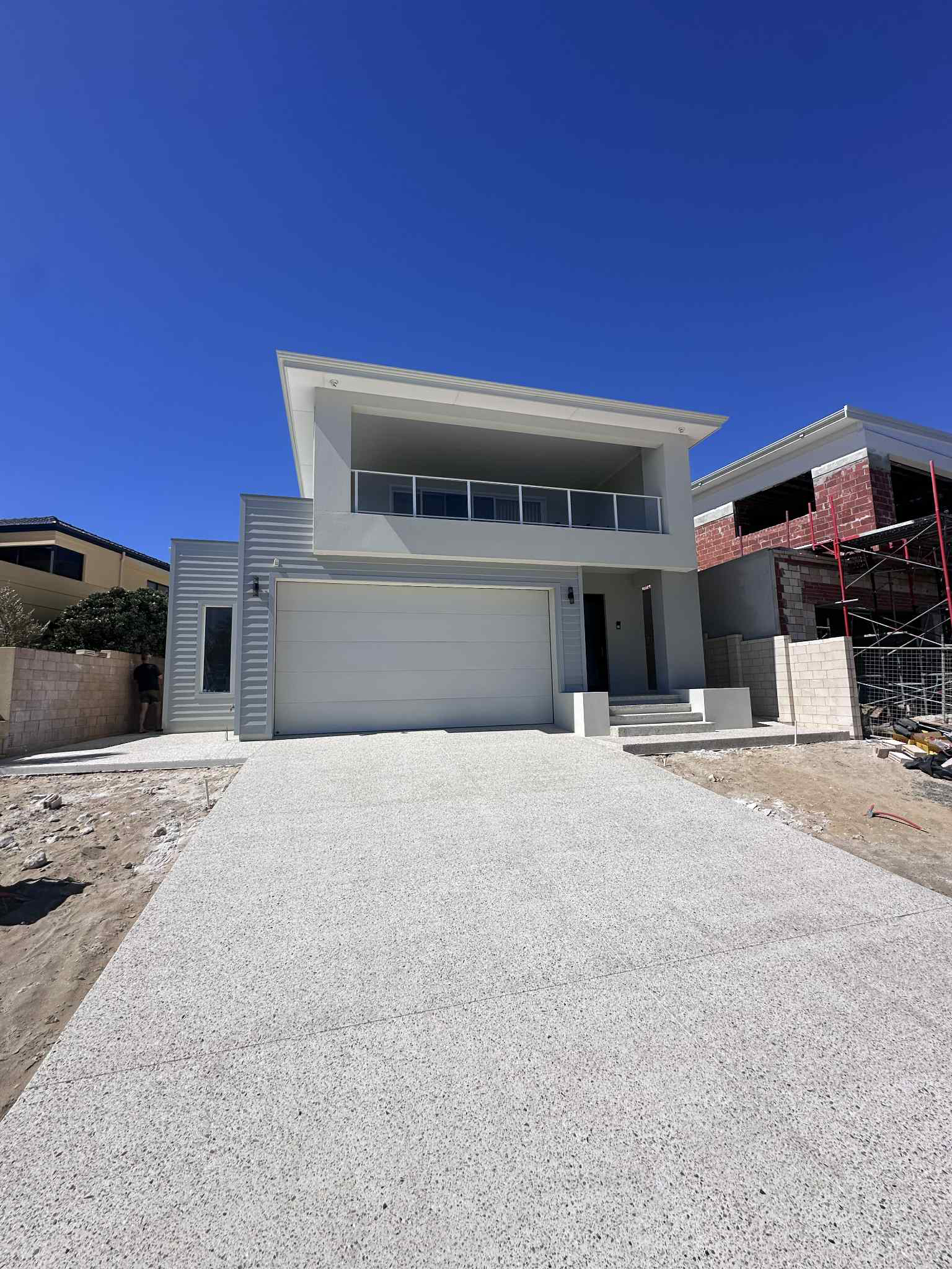 Modern two-story home with a white garage door, driveway of exposed aggregate concrete, and blue sky.
