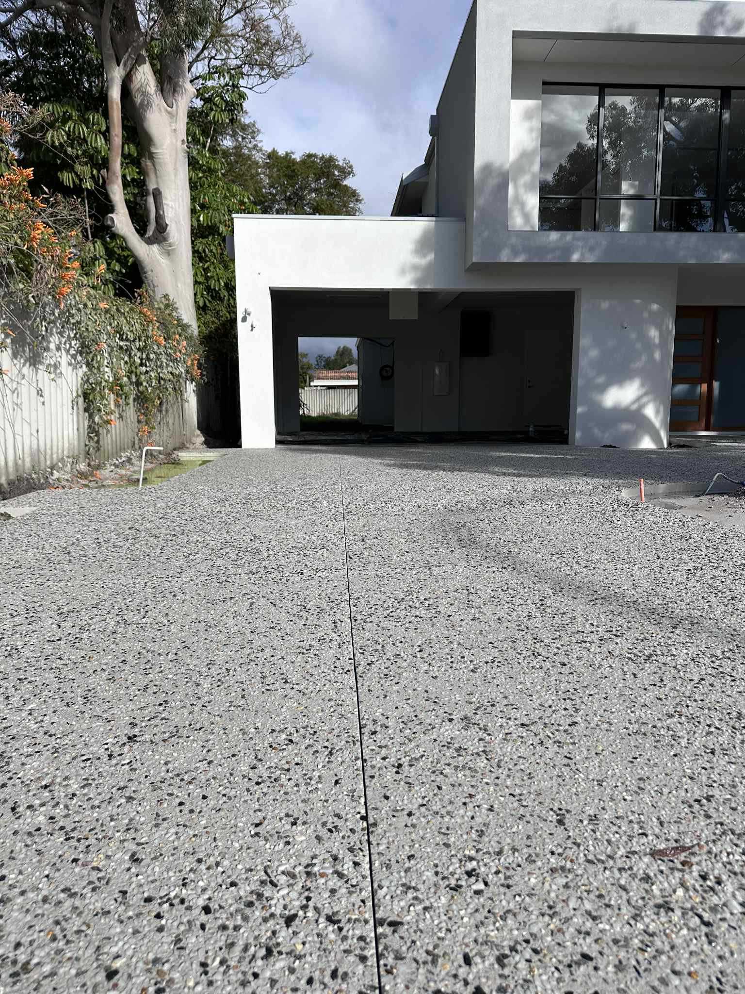 Modern house exterior with a gravel driveway, white walls, and trees on the left.