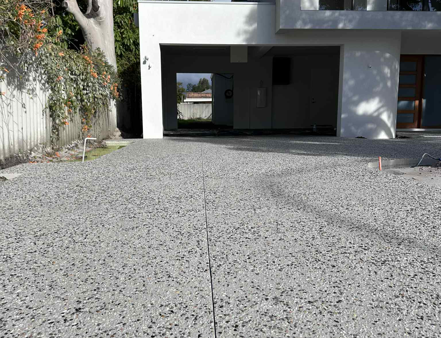 Gravel driveway leading to a white garage with a dark interior and trees along the left side