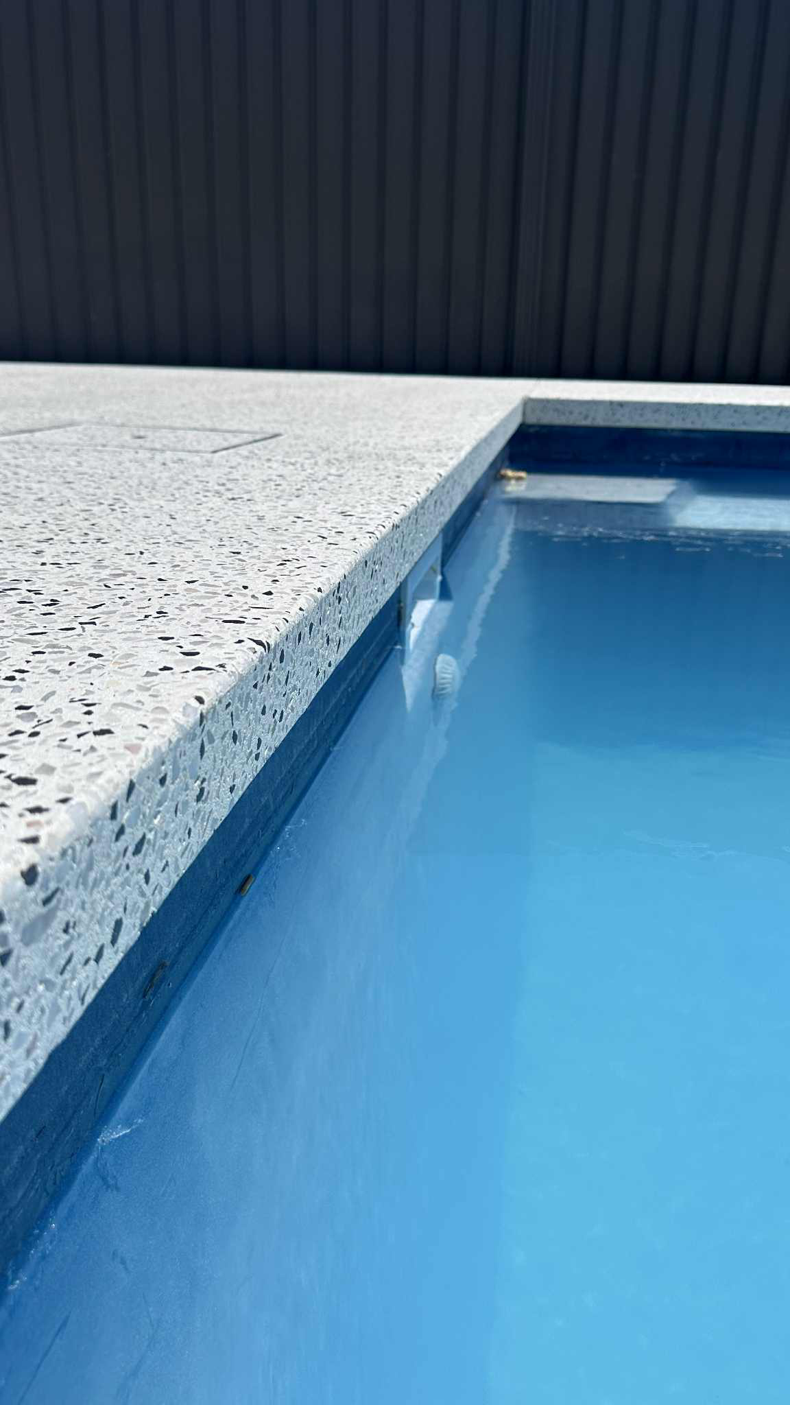 Close up of honed concrete bull noise edging for pool with blue water