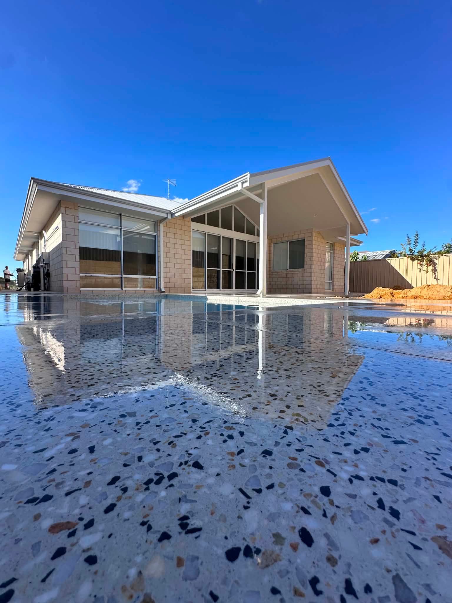 Modern house with a sloped roof and large glass windows reflected on a honed concrete pool area.