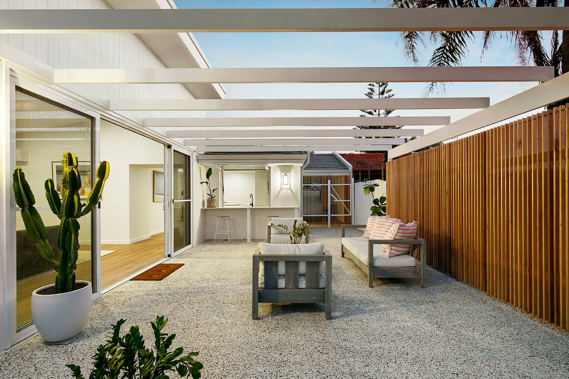 Modern patio with white pergola, honed concrete floor, potted cactus, wooden fence, and outdoor seat
