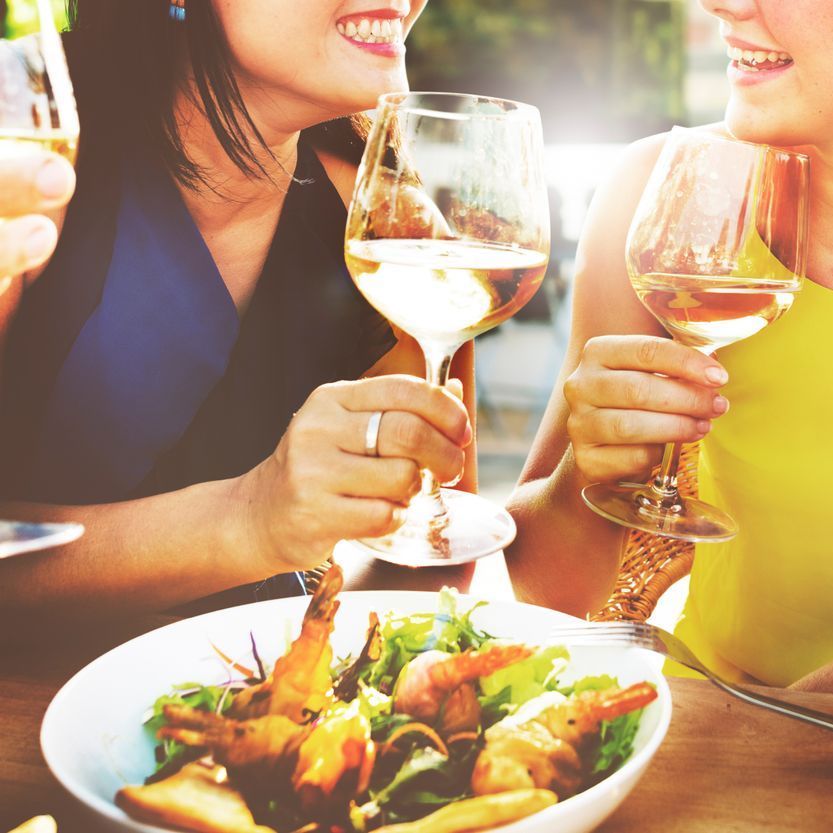 Two women are sitting at a table drinking wine and eating shrimp