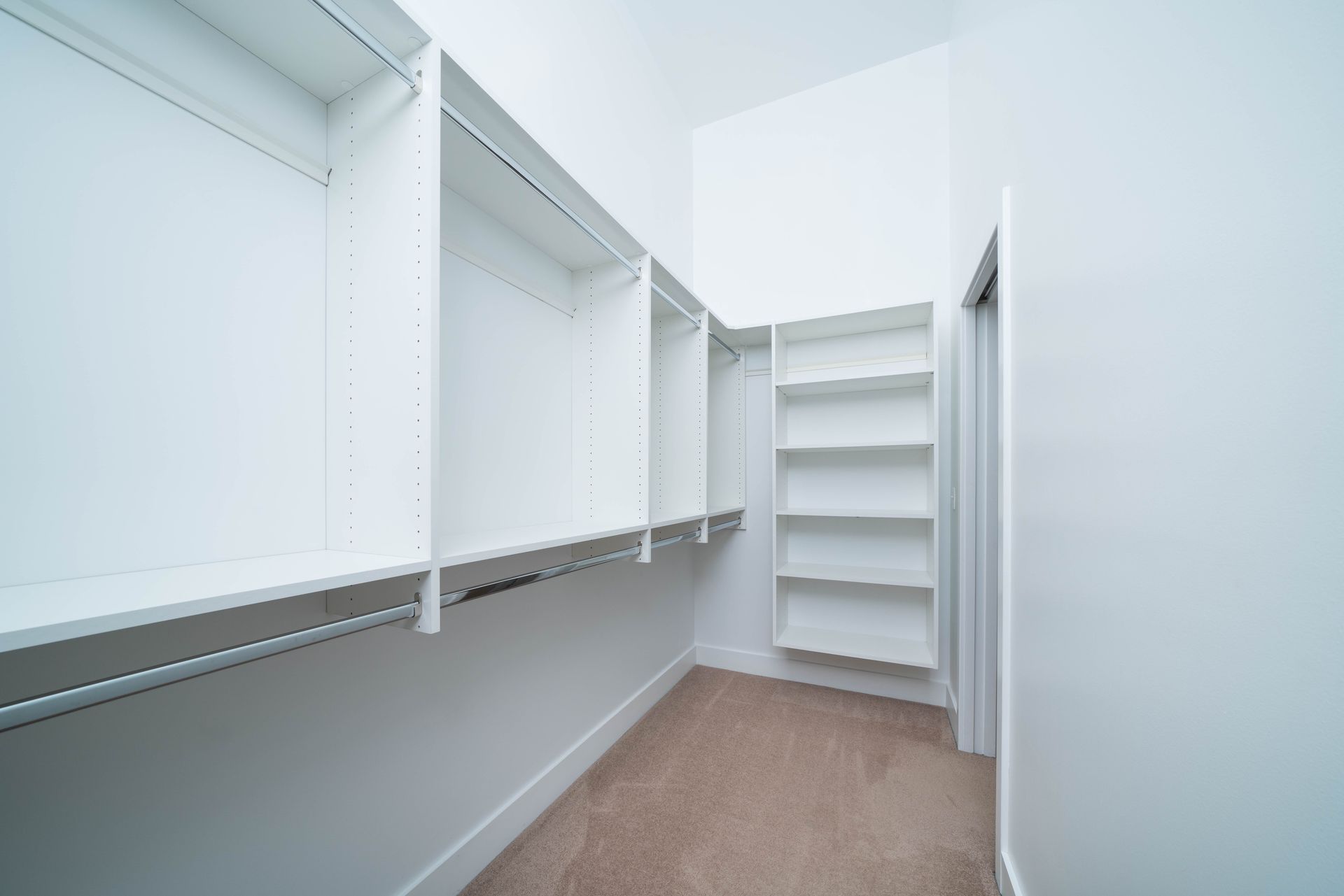 An empty walk in closet with white shelves and a brown carpet.