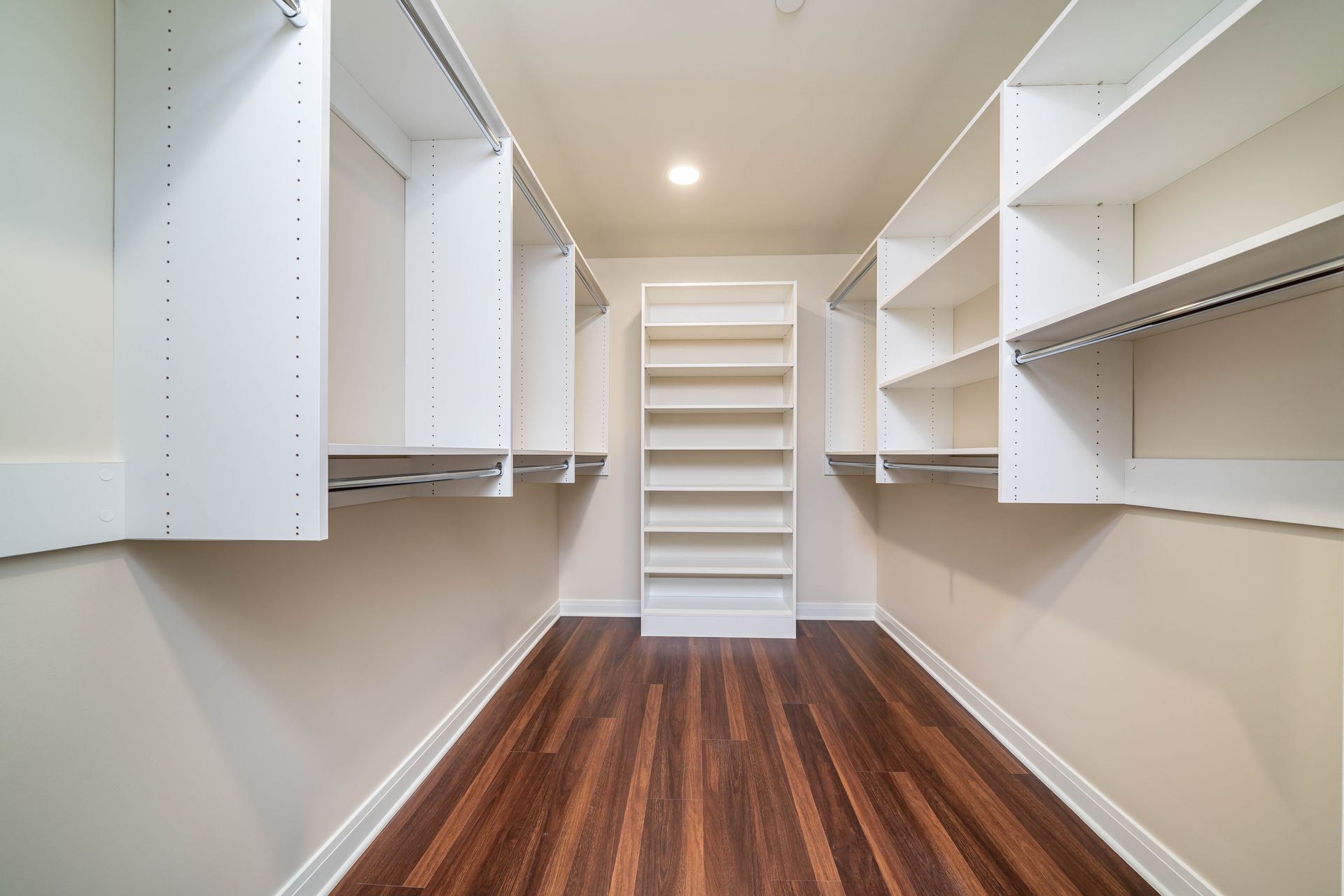 A walk in closet with hardwood floors and white shelves.
