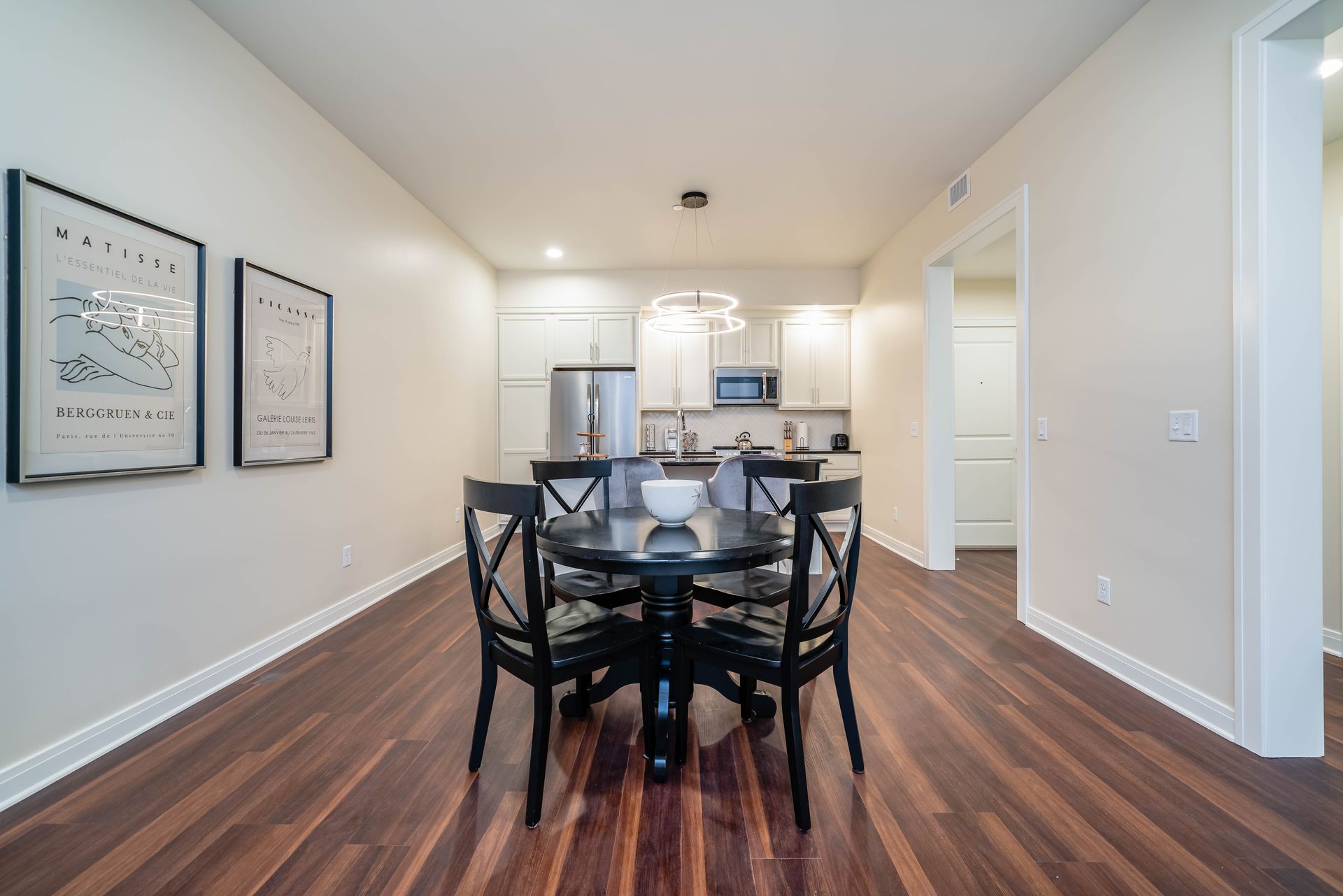 A dining room with a table and chairs and a kitchen in the background.