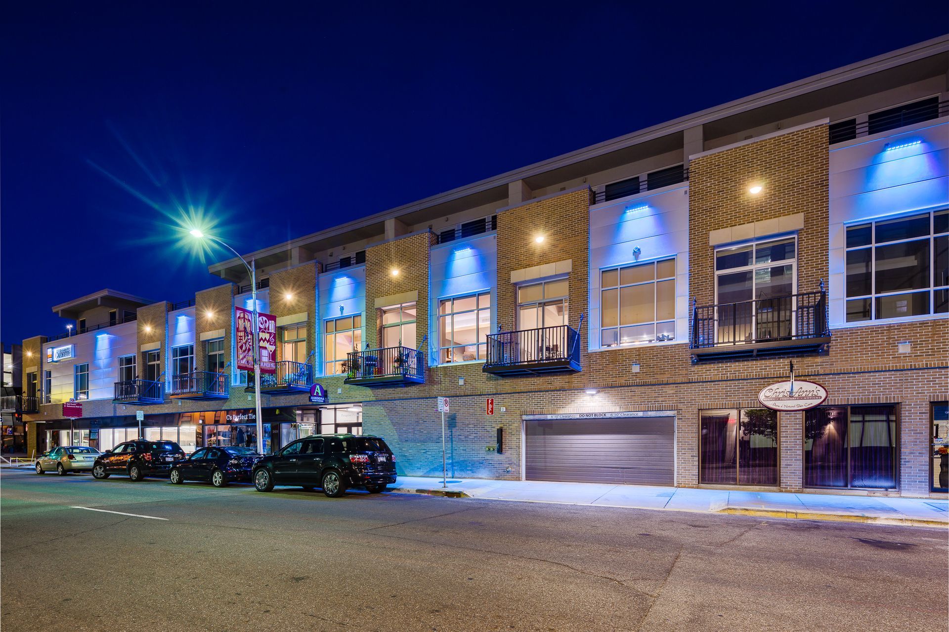 A row of buildings with cars parked in front of them at night.