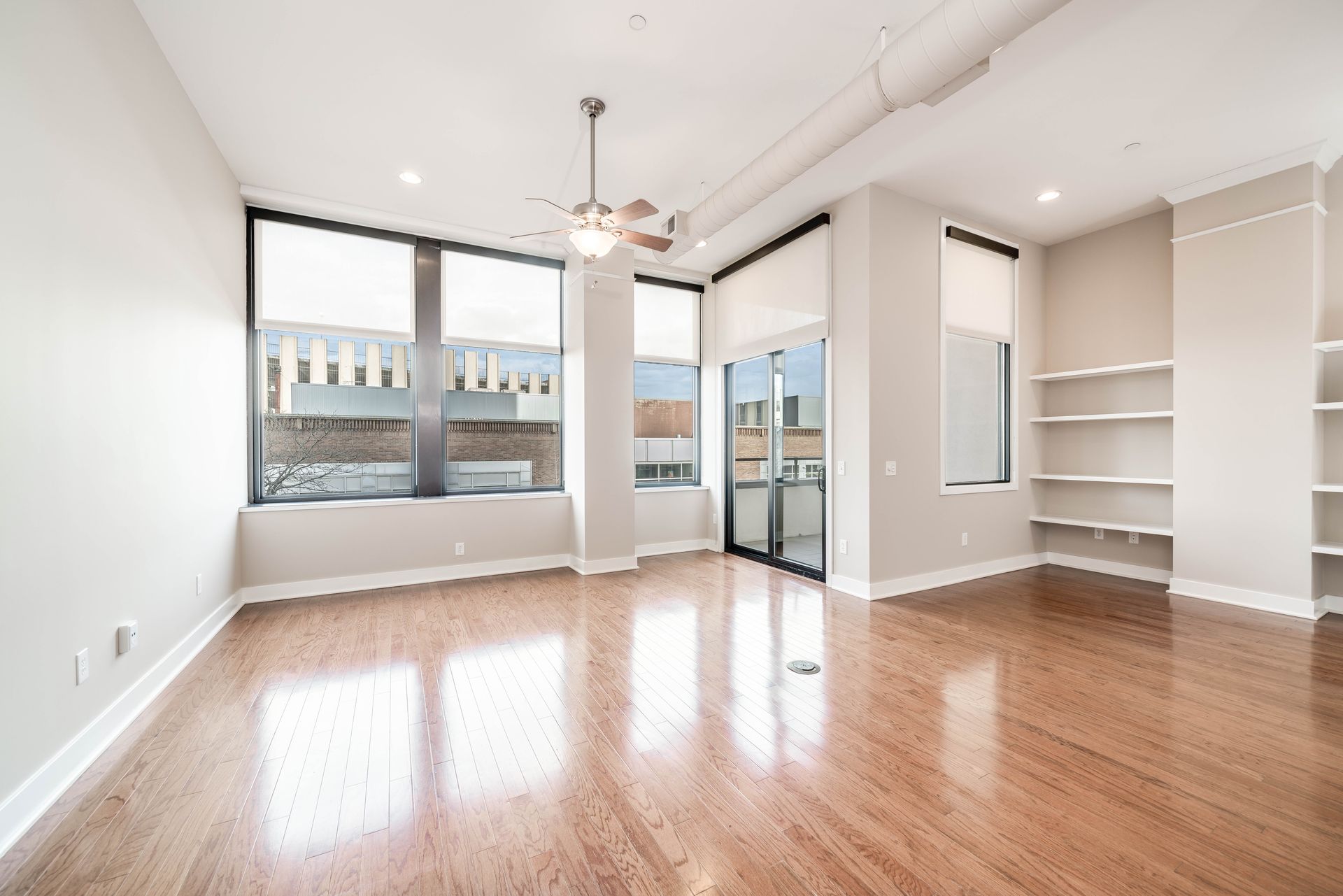 An empty living room with hardwood floors and a ceiling fan