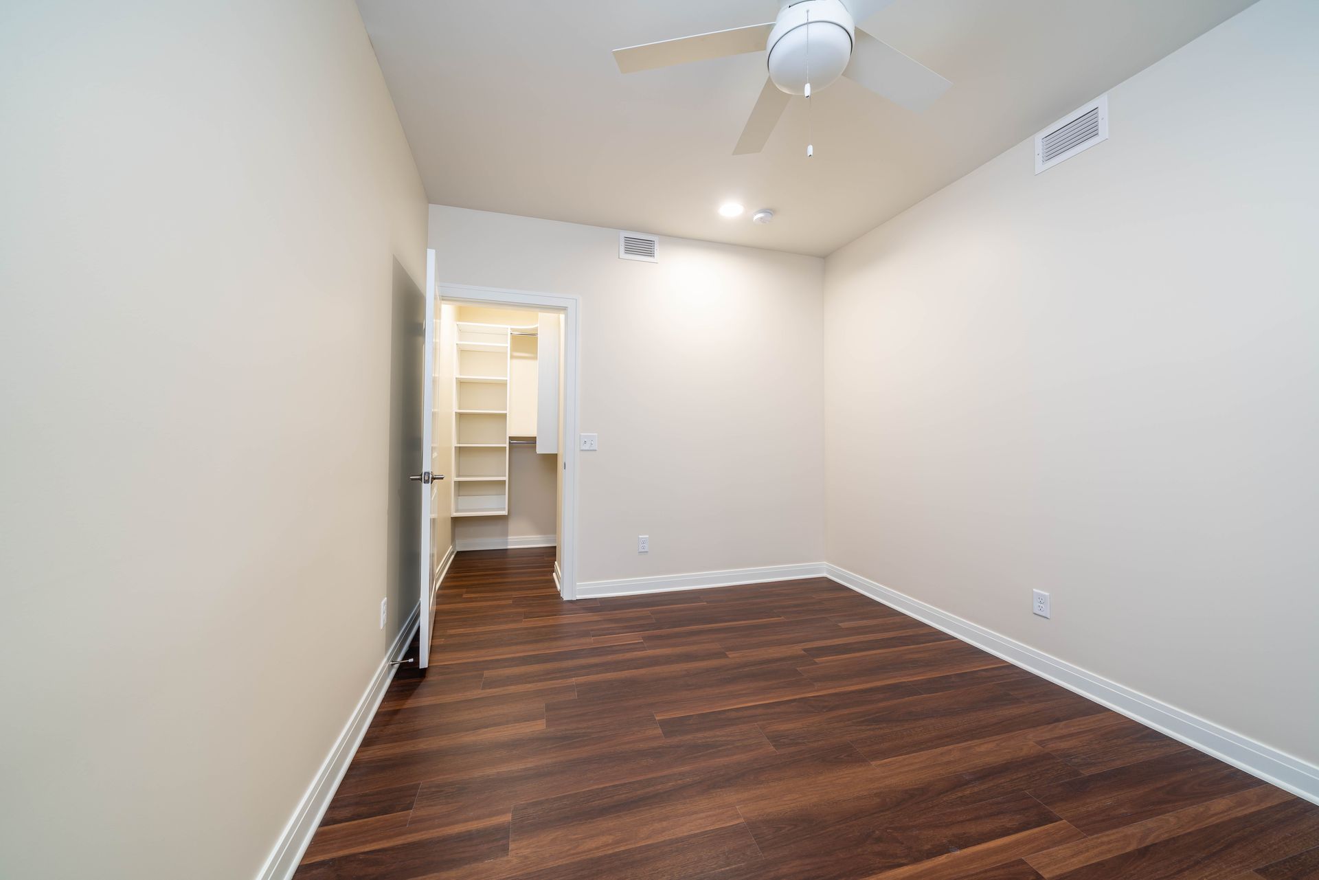 An empty bedroom with hardwood floors and a ceiling fan.
