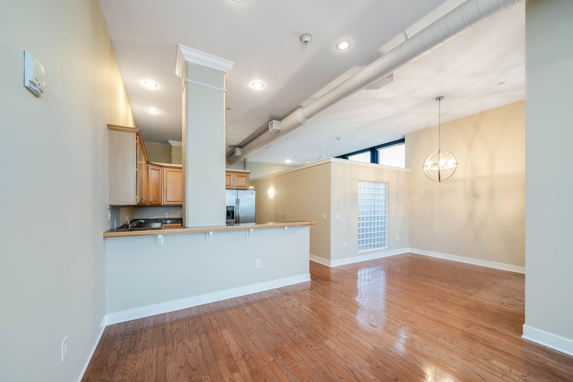An empty living room with hardwood floors and a kitchen in the background.