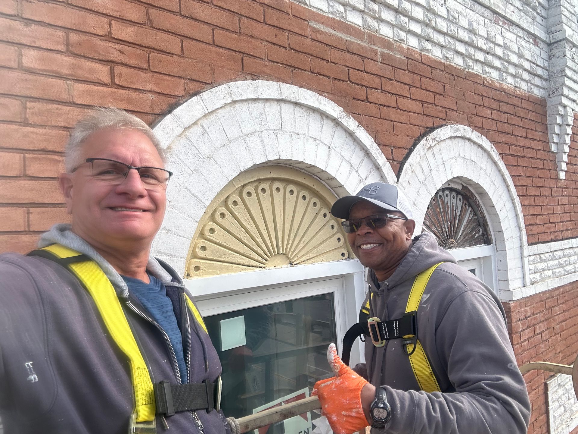 Two men are standing next to each other in front of a brick building.