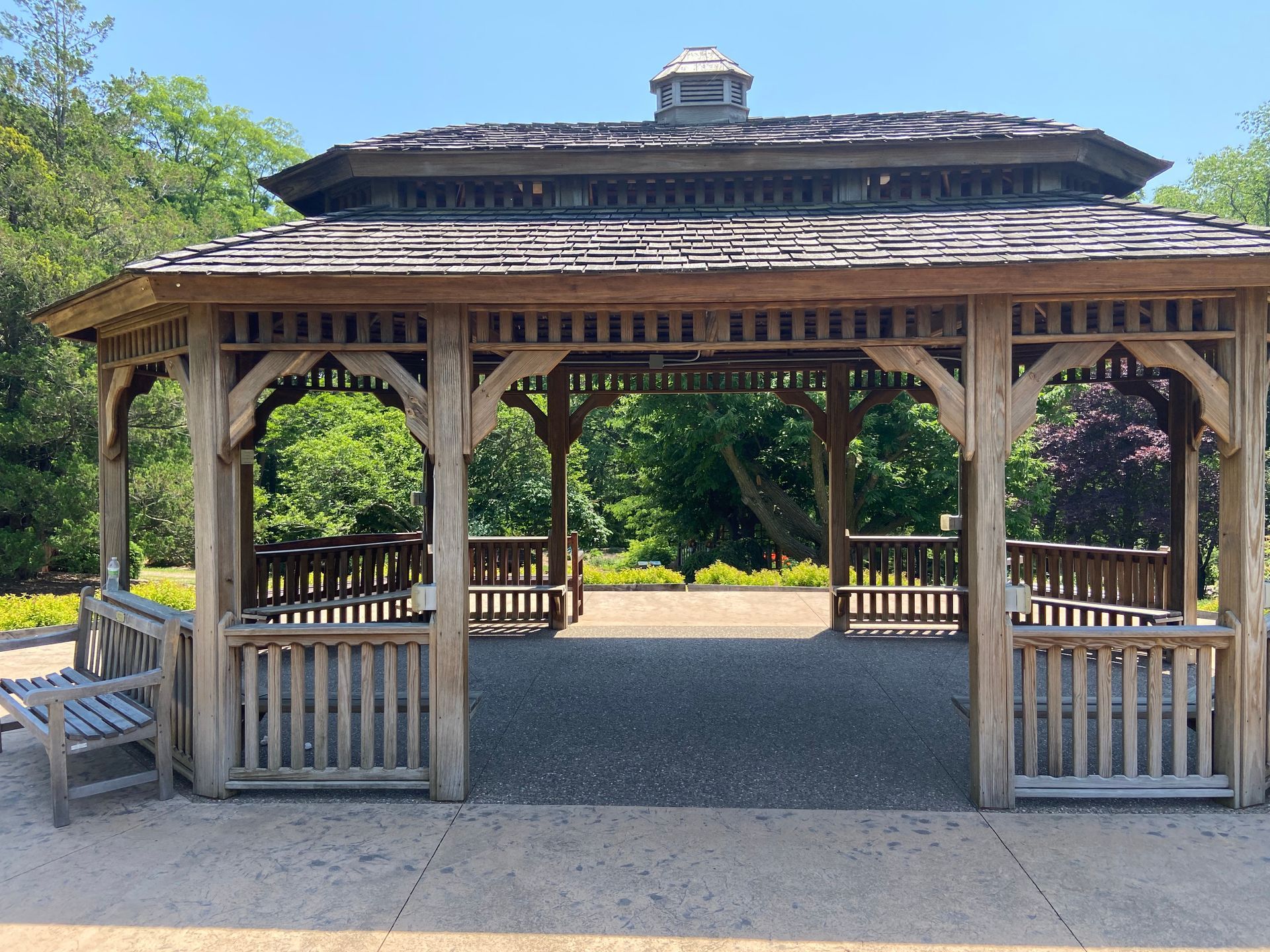 A wooden gazebo with a bench in front of it