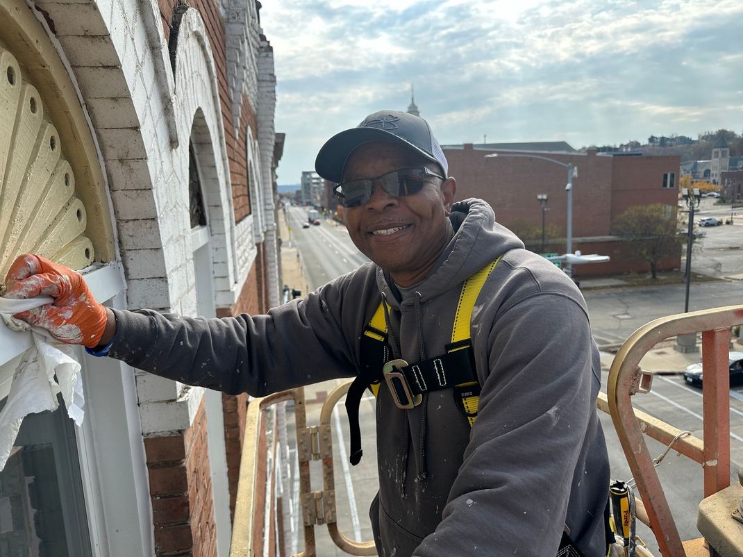 A man is painting a window on the side of a building.