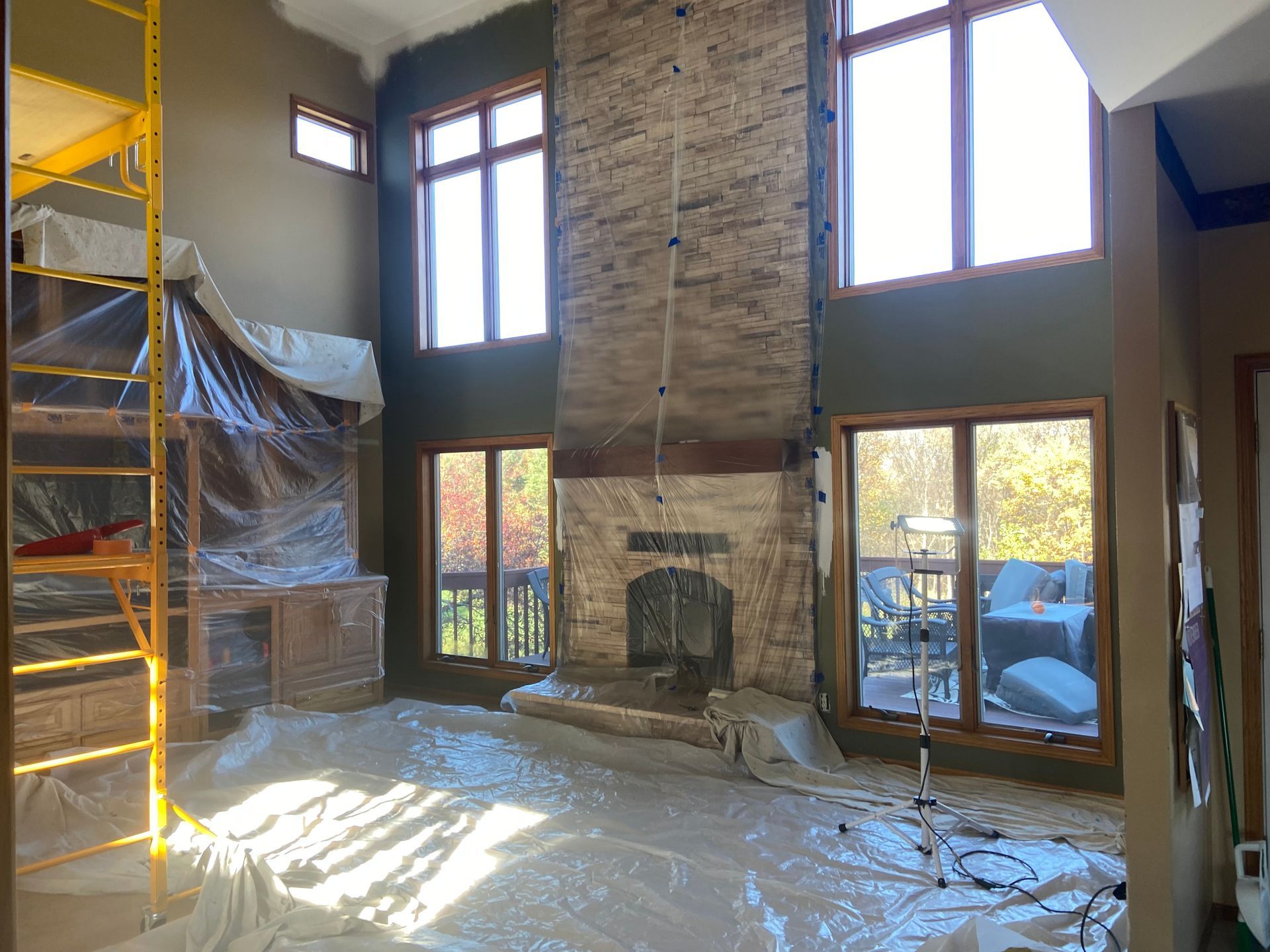 A living room with a fireplace and a lot of windows is being painted.